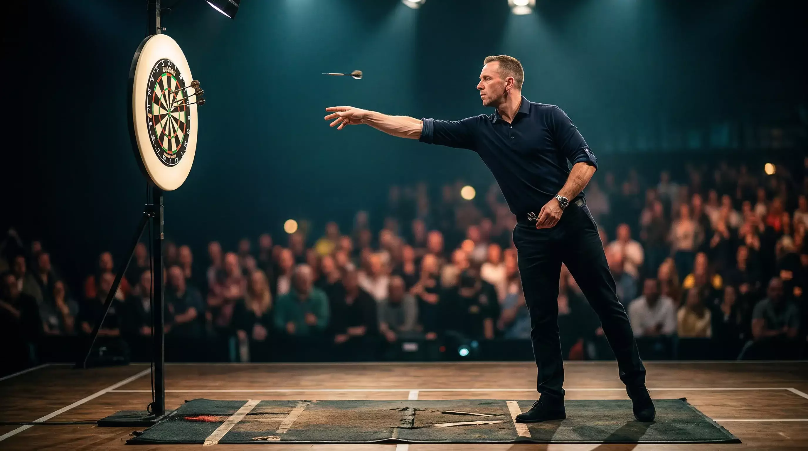 Professioneller Darts-Spieler am Oche beim gezielten Wurf auf die Dartscheibe unter Bühnenlicht